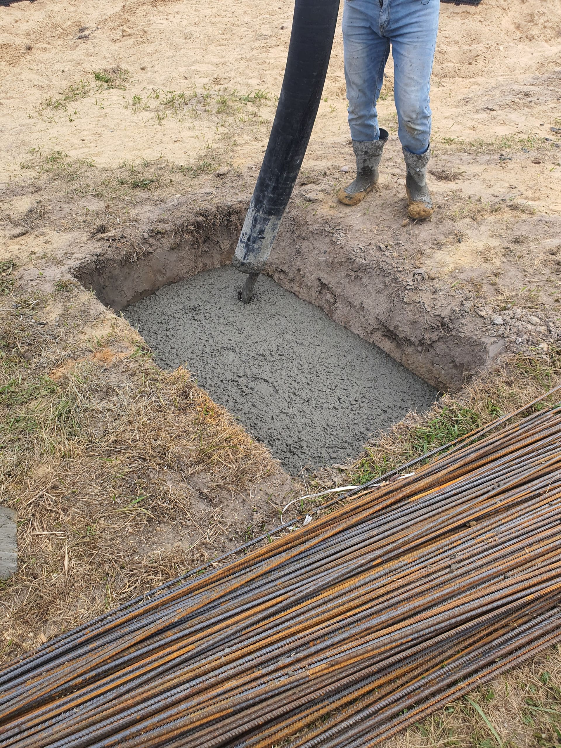 Concrete being placed into a formed footing excavation with rebar staged alongside