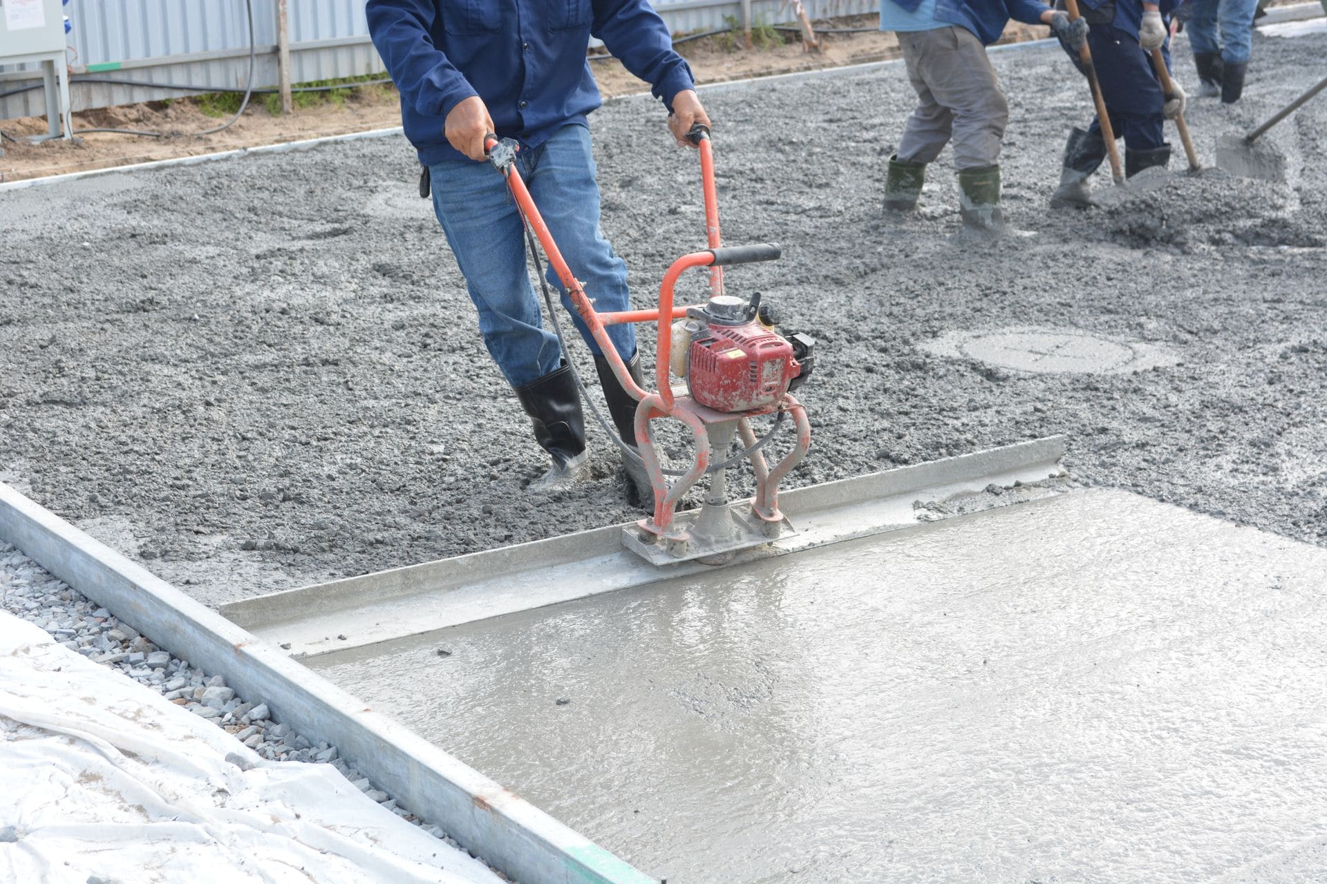 Power screed leveling a freshly poured concrete slab along a curb form