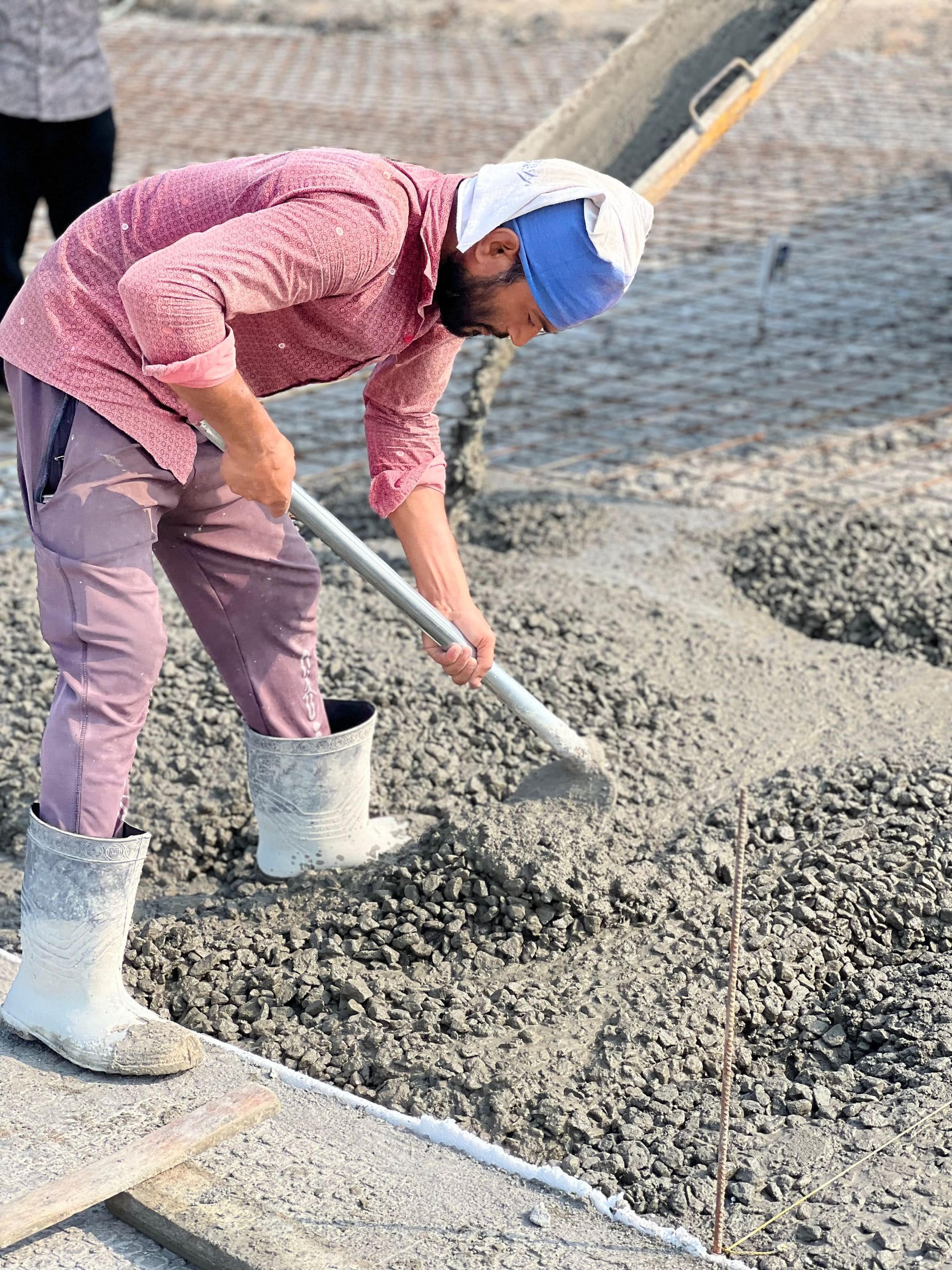 Worker spreading wet concrete across wire mesh reinforcement with a shovel
